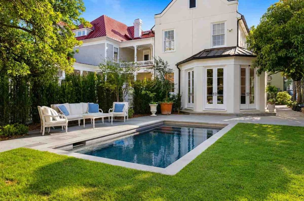 Luxury backyard pool with elegant patio, white seating, and landscaped garden