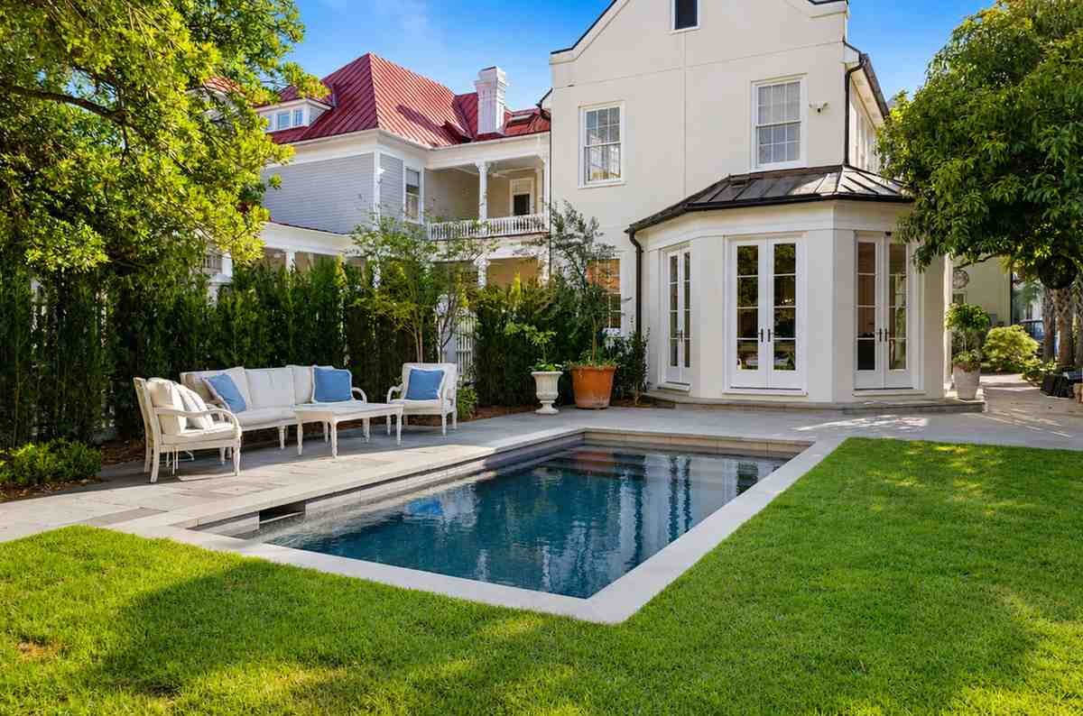 Luxury backyard pool with elegant patio, white seating, and landscaped garden
