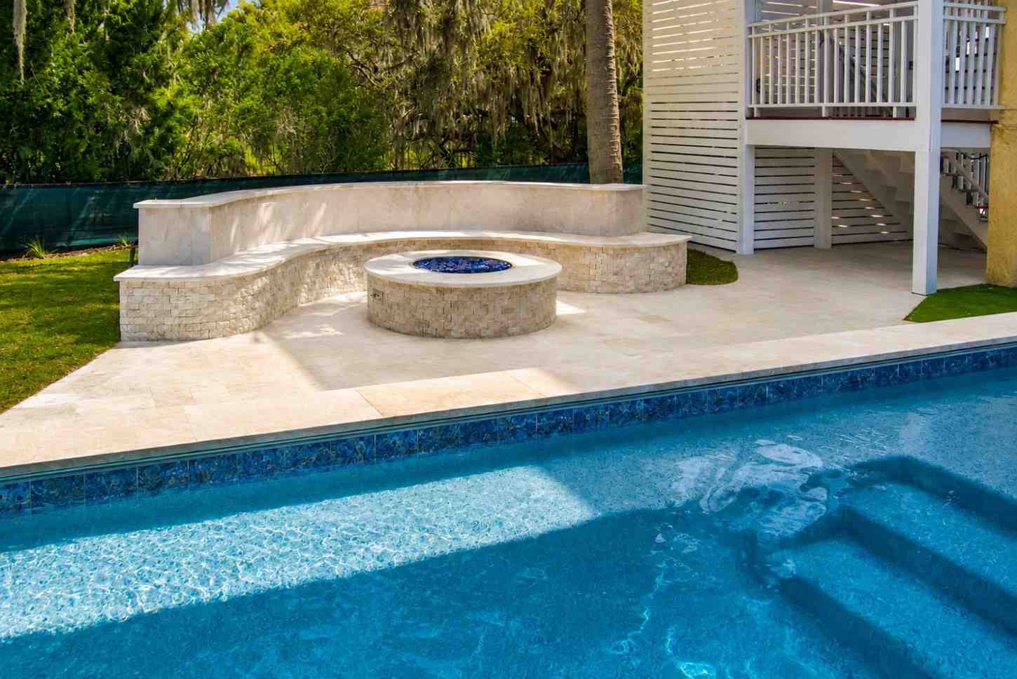 Luxury raised swimming pool with wide stone steps, spacious patio, mature trees, and scenic waterfront backdrop